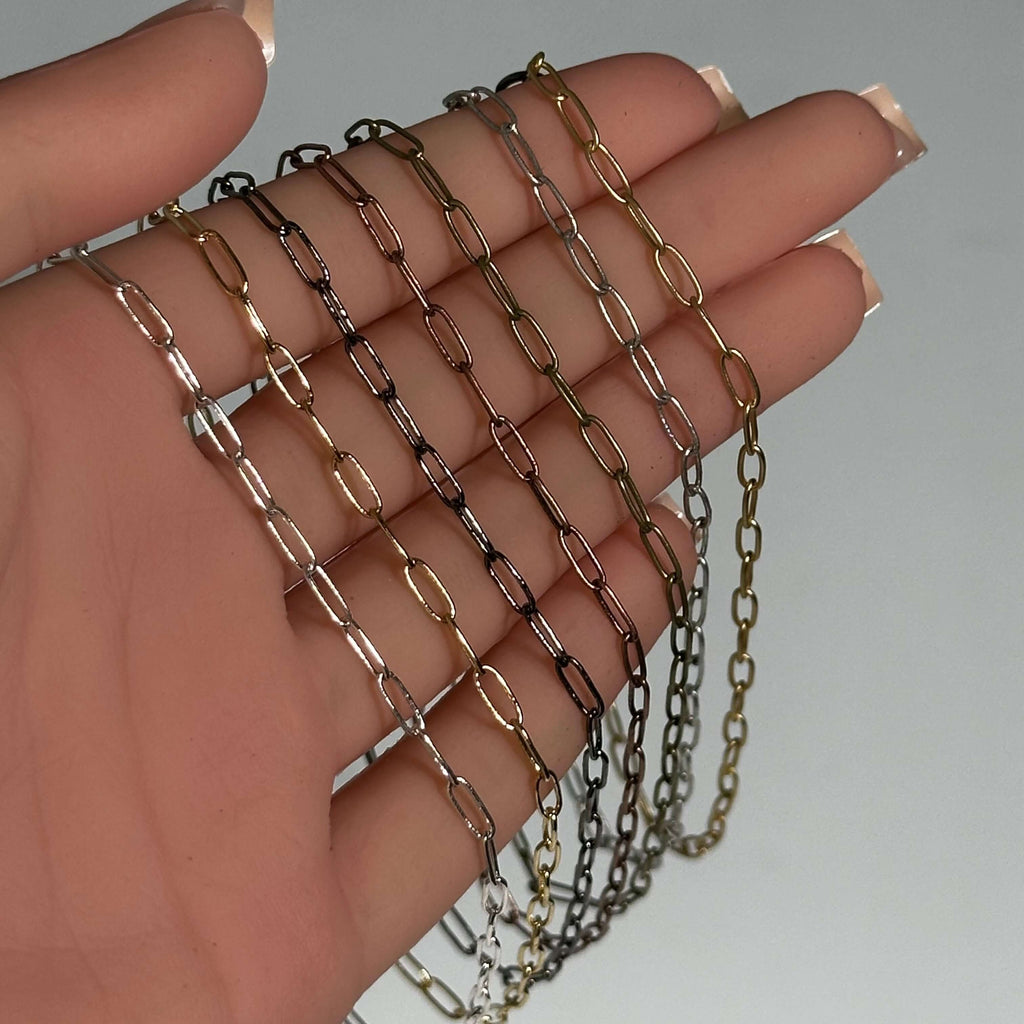 Hand holding small rectangular paperclip chains in multiple colors, showcasing hypoallergenic and nickel-free materials.